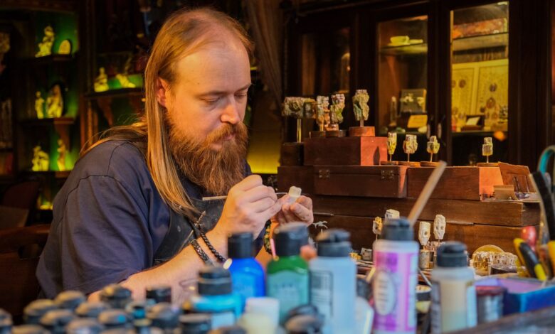 Skilled artisan meticulously painting miniatures in a cozy, cluttered workshop with various vibrant paints.
