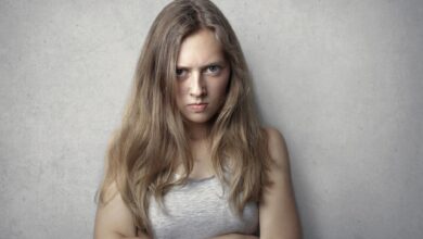 Portrait of a fierce woman with crossed arms and intense expression on a gray background.