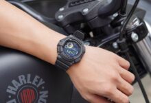 Closeup of a digital watch on a man's wrist, showcasing time on a parked motorcycle.