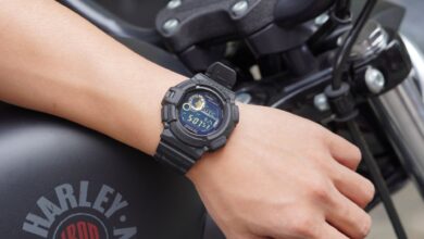 Closeup of a digital watch on a man's wrist, showcasing time on a parked motorcycle.