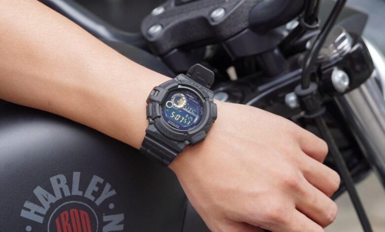 Closeup of a digital watch on a man's wrist, showcasing time on a parked motorcycle.
