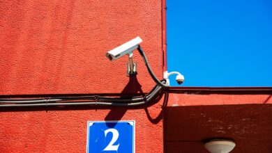 A vivid red wall featuring surveillance cameras and a number sign under a clear blue sky.