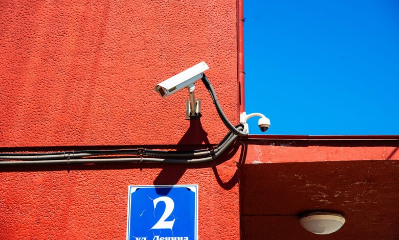 A vivid red wall featuring surveillance cameras and a number sign under a clear blue sky.