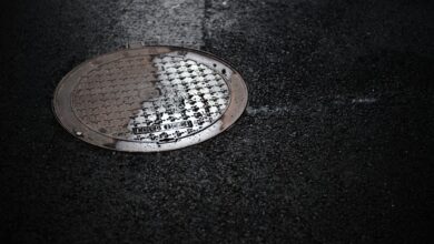 Close-up of a wet manhole cover on a rainy urban street, reflecting light.
