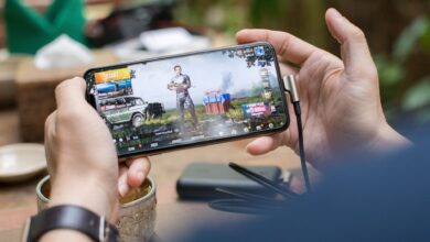 Person playing PUBG on smartphone outdoors with charging cable attached.