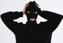 A person in a black balaclava with hands on head creates a mysterious and suspenseful vibe.