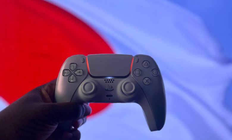 A PlayStation 5 DualSense controller is held up against a backdrop of the Japanese flag.