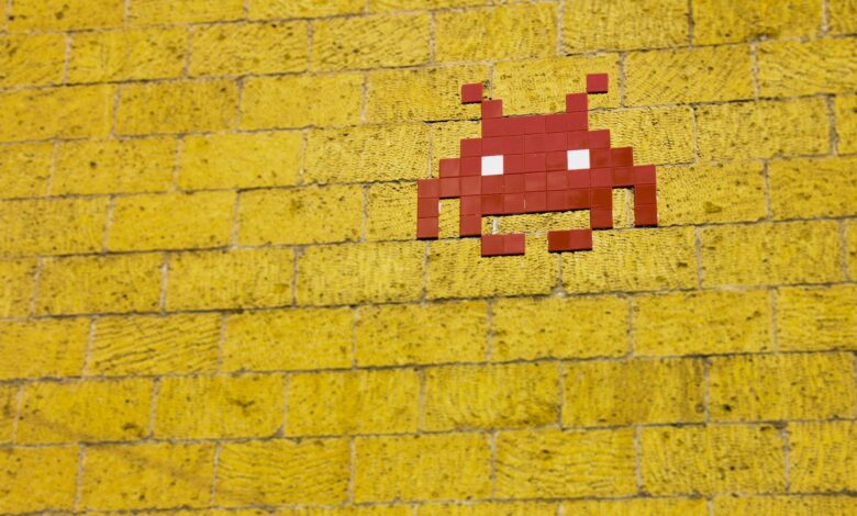 Street art featuring a retro pixelated space invader on a vivid yellow brick wall.