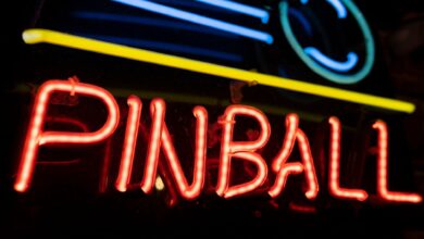 A colorful neon sign illuminating the word 'PINBALL' against a dark background, capturing a retro nightlife vibe.