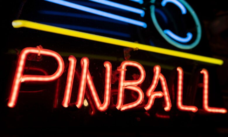 A colorful neon sign illuminating the word 'PINBALL' against a dark background, capturing a retro nightlife vibe.