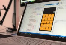 A laptop screen shows a coding application with a calculator design in a tech office setting.