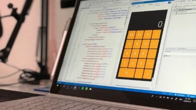 A laptop screen shows a coding application with a calculator design in a tech office setting.