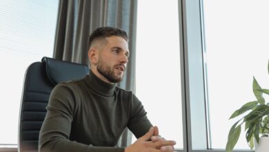 Bearded businessman in turtleneck at work, seated by a bright window.