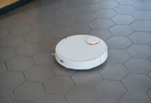 A sleek, white robotic vacuum cleaner operating on a hexagonal tiled floor.