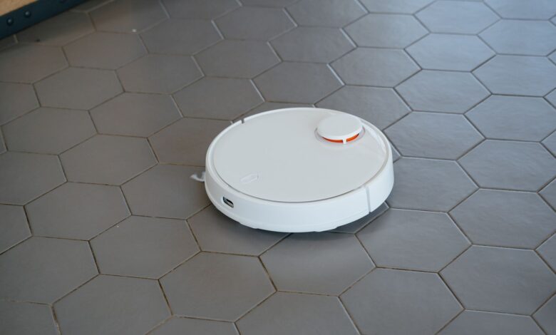 A sleek, white robotic vacuum cleaner operating on a hexagonal tiled floor.