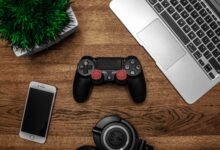 A flat lay photo showcasing a gaming console, laptop, smartphone, and headphones on a wooden tabletop.