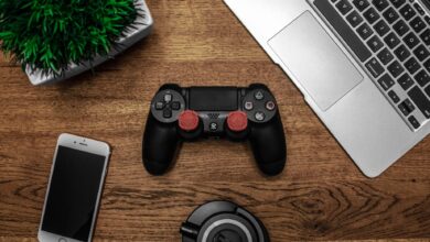 A flat lay photo showcasing a gaming console, laptop, smartphone, and headphones on a wooden tabletop.