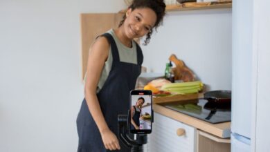 Smiling young woman films a cooking video at home using a smartphone in her kitchen.