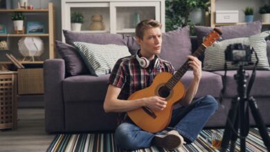 Man sitting cross-legged playing acoustic guitar indoors, streaming online.