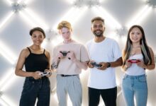 A diverse group of young adults smiling and holding game controllers indoors.