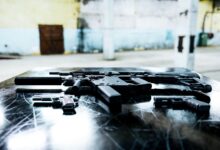 Various firearms displayed on a scratched metal table in an industrial setting.