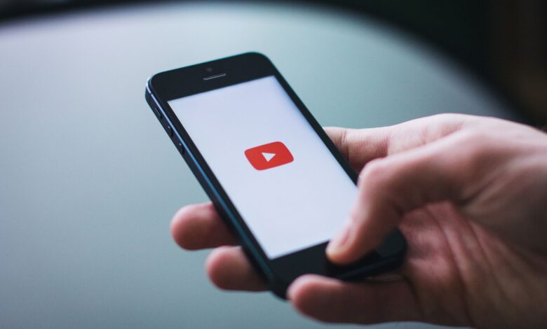 Close-up of a hand holding a smartphone displaying the YouTube app on the screen.