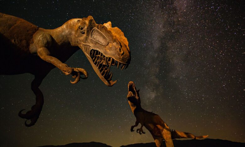 Silhouetted dinosaur statues under a vivid Milky Way night sky.