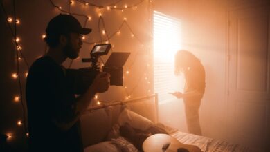 A filmmaker captures a scene in a dimly lit bedroom with string lights.