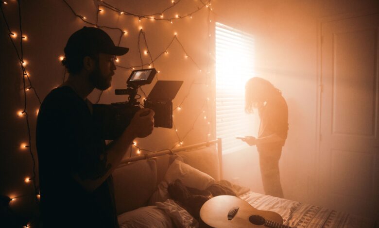 A filmmaker captures a scene in a dimly lit bedroom with string lights.