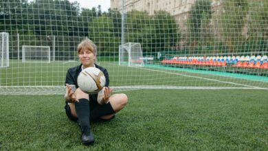 A female soccer player sitting with a ball on a soccer field, enjoying a break.