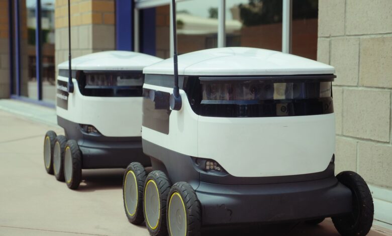 Two autonomous delivery robots positioned outside a modern building, showcasing innovation in robotics and mobility.