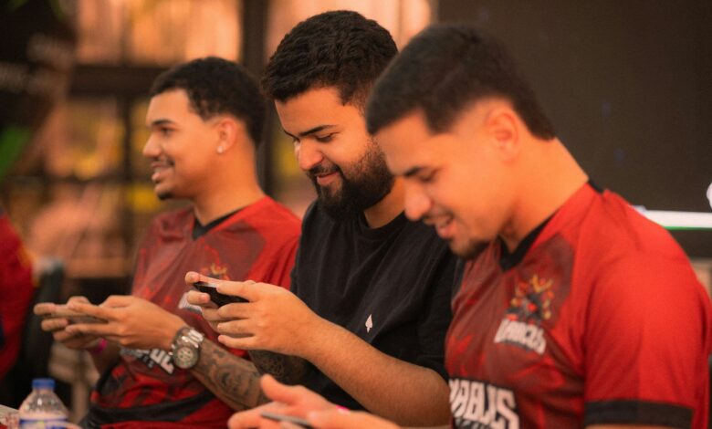 Three young men focus intensely on a mobile gaming competition indoors.