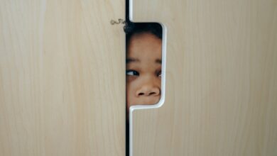 Anonymous funny little ethnic child hiding in wardrobe and peeping through hole while playing at home