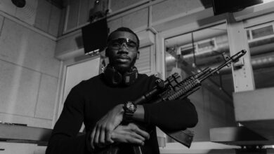 Black and white image of a man with a rifle at a shooting range, wearing safety equipment.