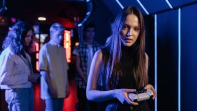 A young woman holding a game controller in a neon-lit arcade, surrounded by friends.