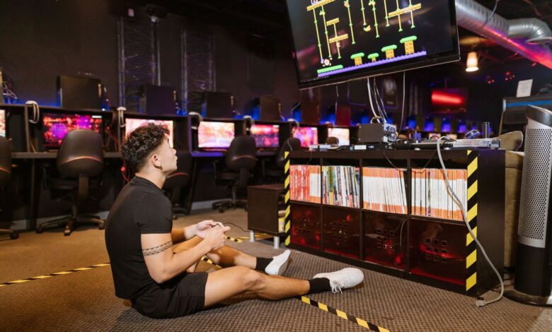 Man sitting on floor intensely playing video game at a modern arcade with vibrant computing equipment.