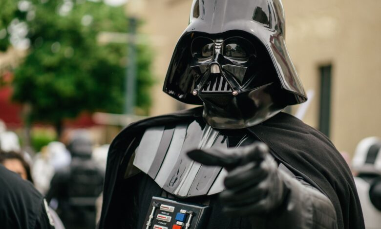 Darth Vader cosplayer pointing in an outdoor setting, showcasing detailed costume and helmet.