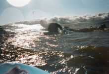 A surfer paddles through shimmering ocean waves under a glowing sunset, capturing a moment of pure adventure.