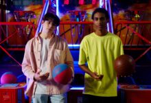 Two young men holding basketballs at an amusement arcade, engaging in a fun indoor game.