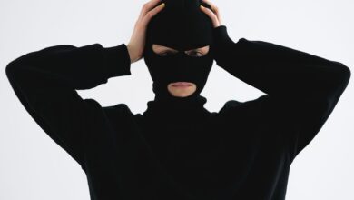 A person in a black balaclava with hands on head creates a mysterious and suspenseful vibe.