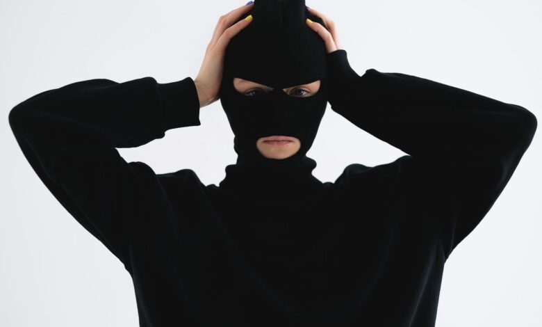 A person in a black balaclava with hands on head creates a mysterious and suspenseful vibe.