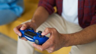 Hands holding a blue wireless game controller on a comfortable sofa indoors.