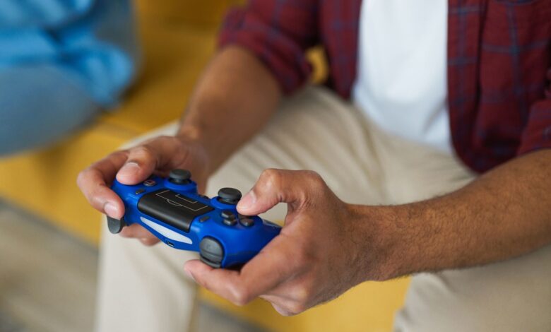 Hands holding a blue wireless game controller on a comfortable sofa indoors.