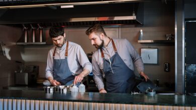 Two male chefs in aprons cook attentively in a contemporary open kitchen setting.
