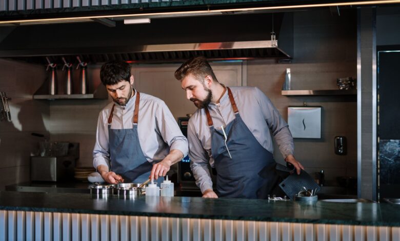 Two male chefs in aprons cook attentively in a contemporary open kitchen setting.