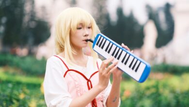 A young woman in cosplay costume beautifully playing a melodica in a vibrant outdoor garden setting.
