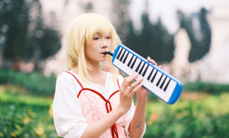 A young woman in cosplay costume beautifully playing a melodica in a vibrant outdoor garden setting.