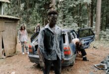 A chilling zombie scene unfolds by an abandoned car in a dense forest.