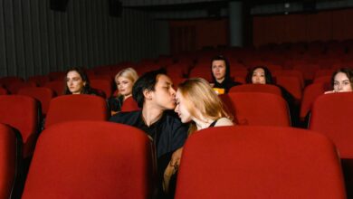 A couple shares a romantic kiss in an empty movie theater, captured from the front.