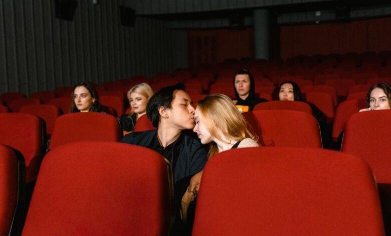 A couple shares a romantic kiss in an empty movie theater, captured from the front.